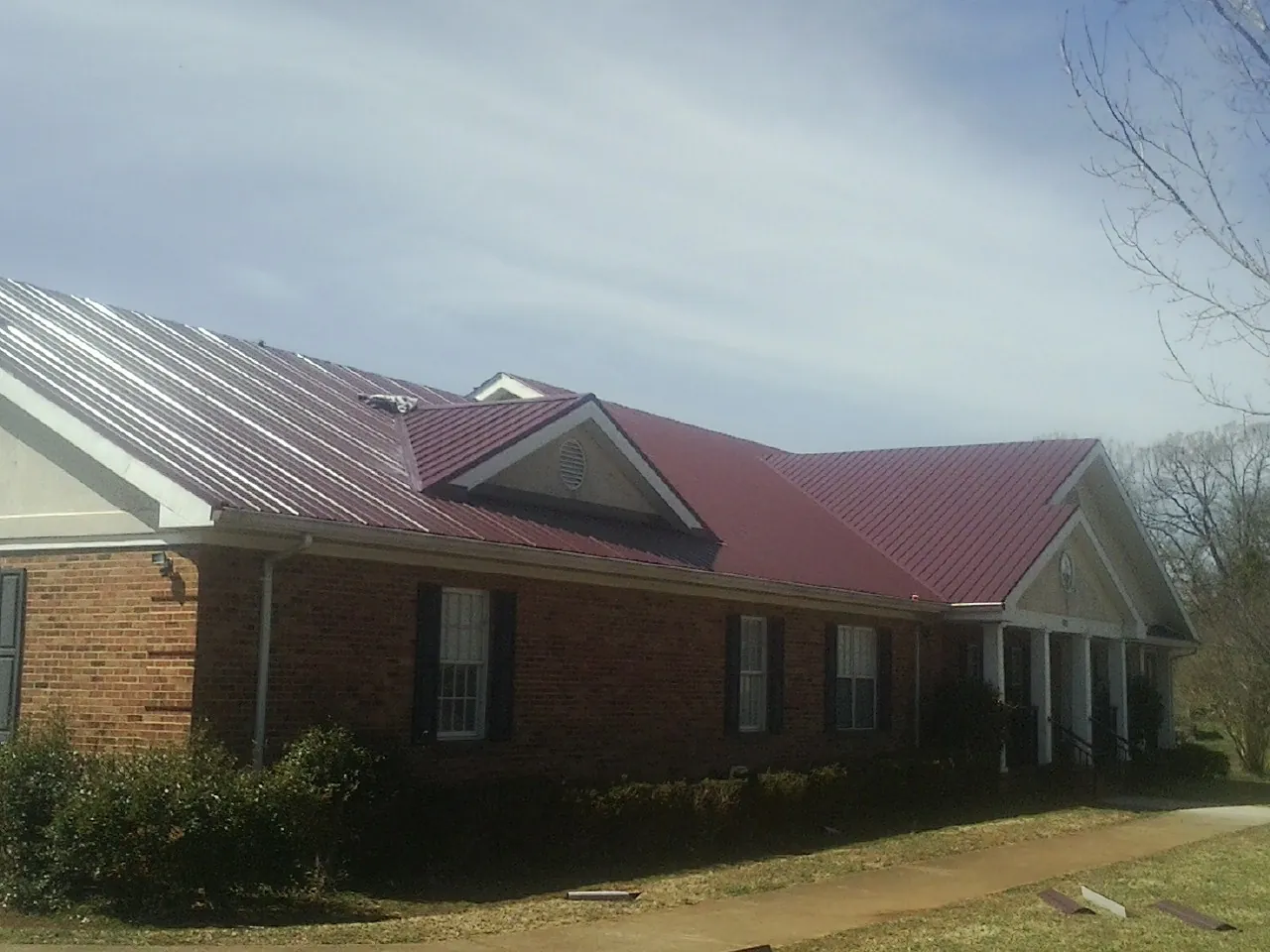 Red metal roof with gabled entries on a long brick building, from a Hail Damage Roof Repair job in Oregon City