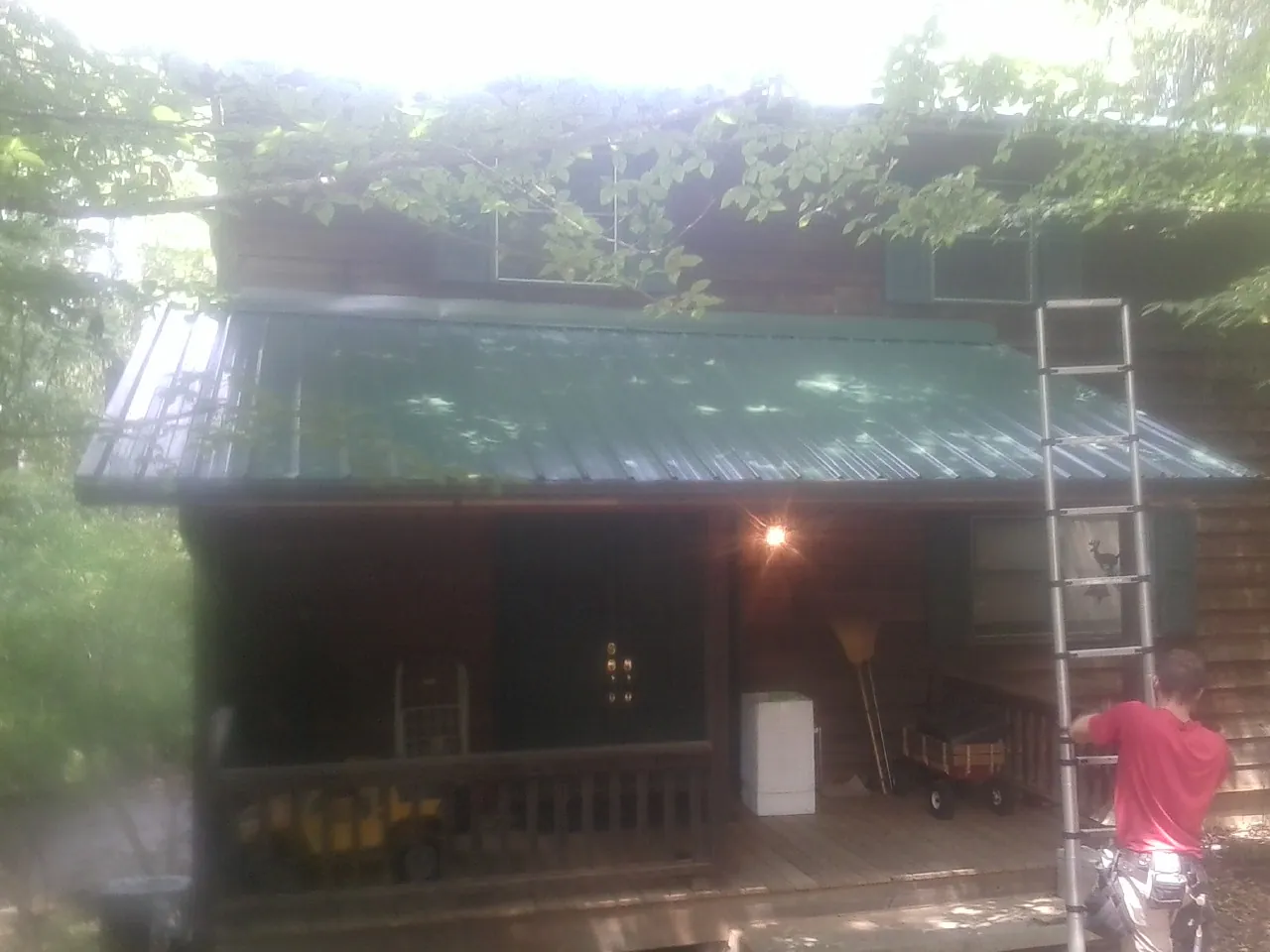 Worker on a ladder at the green porch roof of a wooded cabin in Oregon City