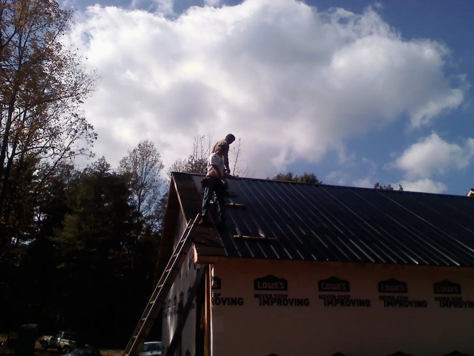 Roofer fastening dark metal panels high against a cloudy sky, from a Roof Inspection job in Oregon City