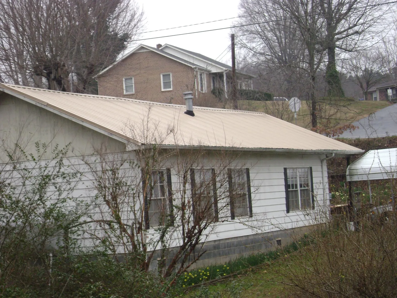Tan metal roof on a white sided house set into a hillside — Commercial Roofing by Roofing Brothers in Oregon City